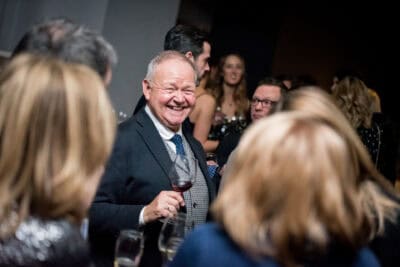 A man in a suit and tie drinking wine at a party.