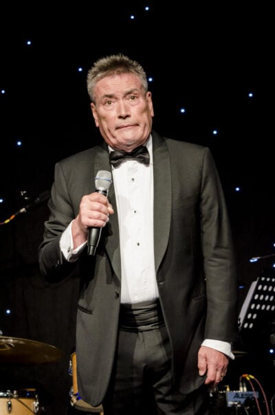 A man in a tuxedo holding a microphone.