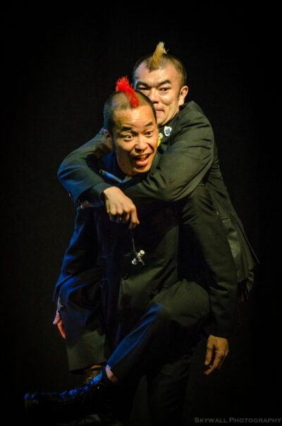 Two men in black suits hugging each other on stage.
