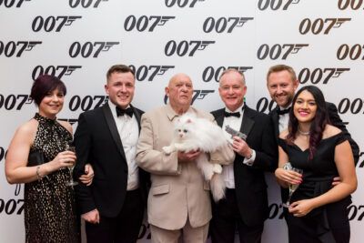 A group of people posing with a white cat in front of the james bond logo.