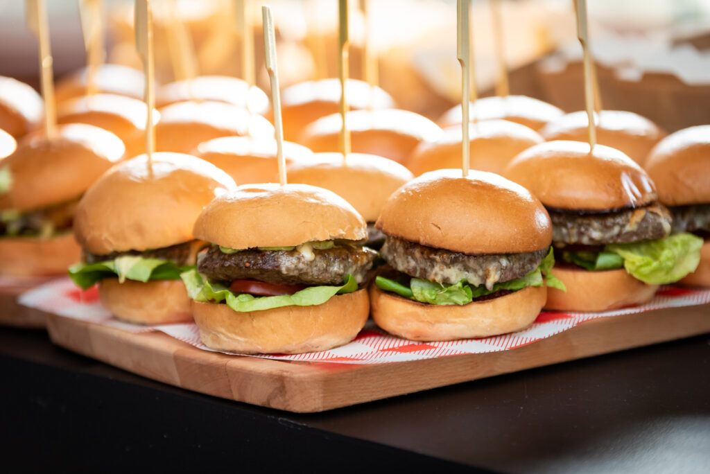 Burger sliders on a wooden tray with toothpicks.