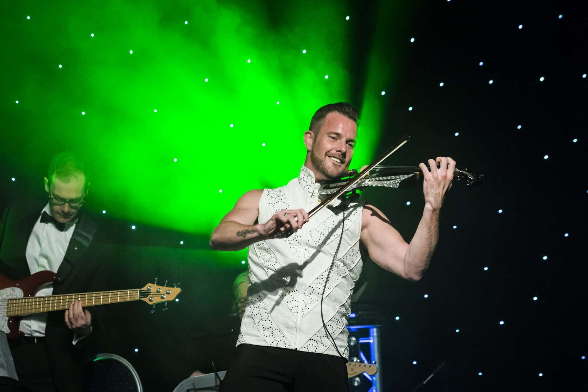 A man playing violin on stage in front of green lights.