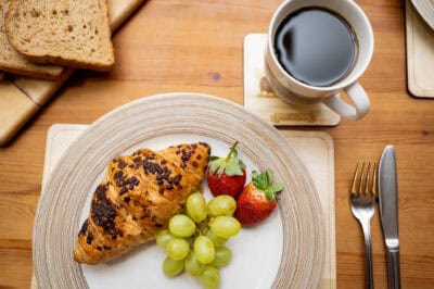 A plate with a croissant, grapes and a cup of coffee.