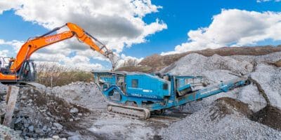 A blue and orange excavator is working on a pile of rocks.