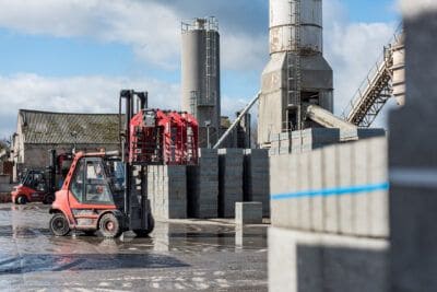 A red forklift is parked in front of a cement factory.