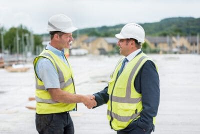 Two construction workers shaking hands in front of a construction site.