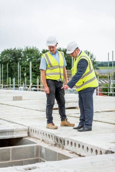 Two construction workers standing on a concrete floor.