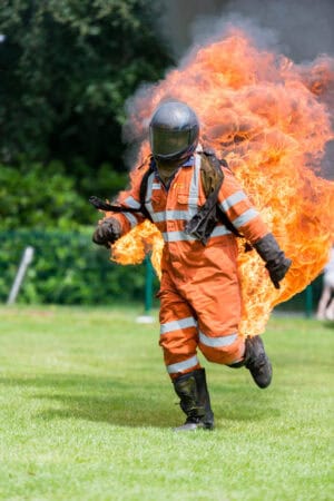 A firefighter running through a field with flames.