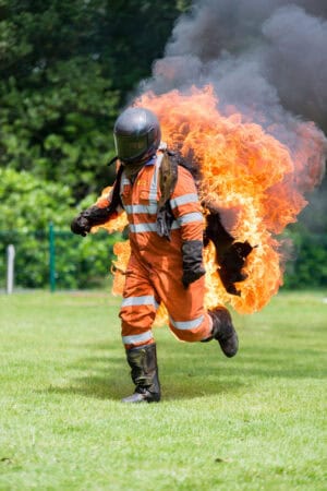 A firefighter running through a field with flames.