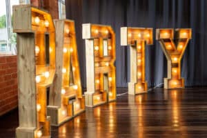 Lighted letters spelling out the word party on a wooden floor.