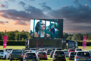 A large screen with cars parked in front of it.