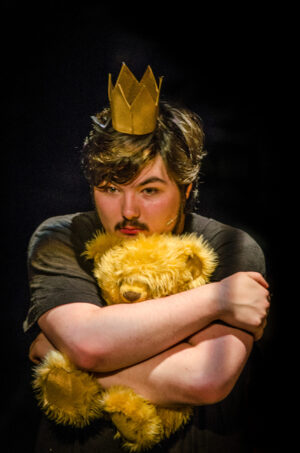 A man wearing a crown and hugging a teddy bear.
