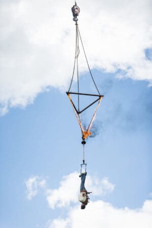 A man is hanging from a crane in the sky.