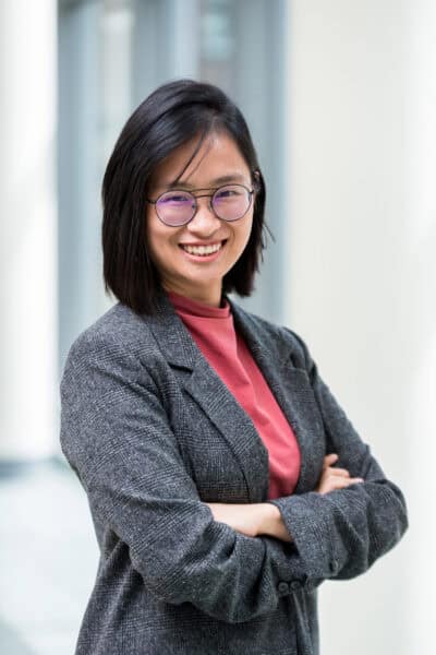 A smiling asian woman wearing glasses and a suit.