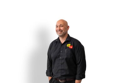 A bald man in a black shirt standing in front of a white background.