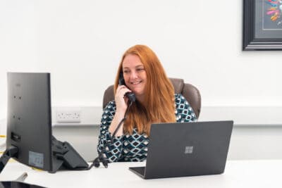 A woman talking on a phone while sitting at a desk.