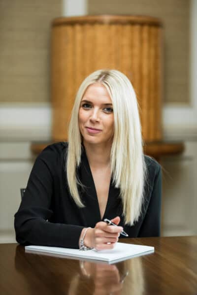 A blond woman sitting at a desk with a pen.