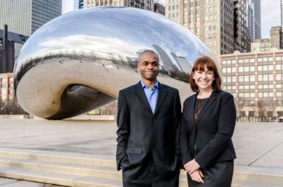 Two people standing in front of a cloud gate sculpture.
