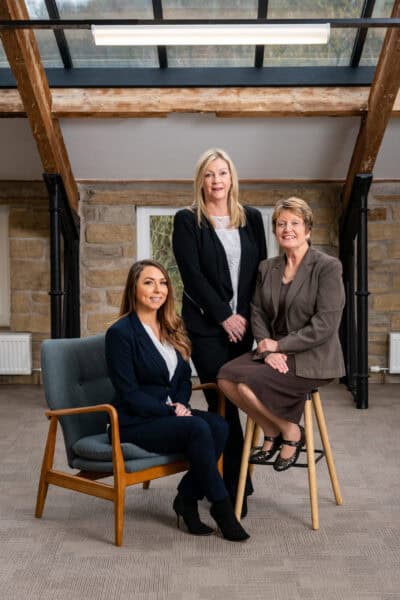 Three women in business attire posing for a photo in an office.