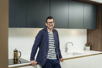 A man in glasses standing in front of a kitchen.