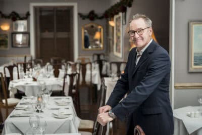 A man in a suit leaning against a table in a restaurant.
