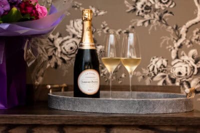 A bottle of champagne sits on a tray with flowers.