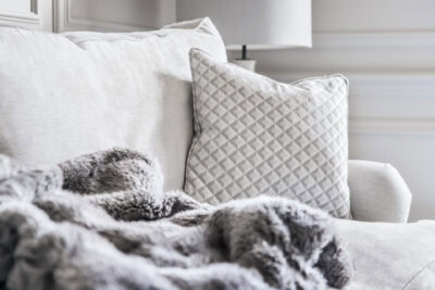 A white couch with a grey throw blanket.
