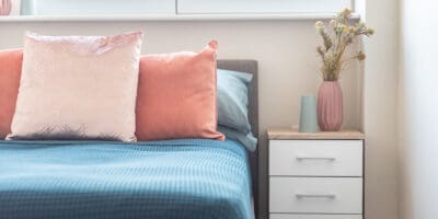 A bed with pink and blue pillows and a blue dresser.