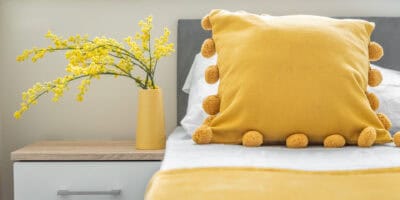 A yellow pom pom pillow on a bed.