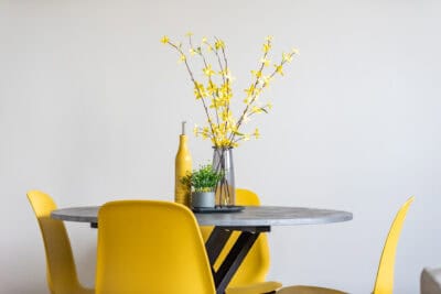 A table with yellow chairs and a vase of flowers.