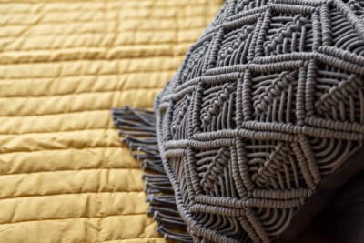 A grey and yellow pillow on top of a yellow quilt.