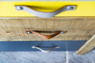 A close up of a yellow and blue dresser with leather handles.