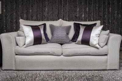A white sofa with purple pillows in front of a black wall.