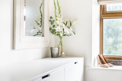 A white dresser with a vase of flowers next to a window.