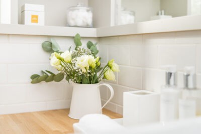 A white bathroom with a vase of flowers and a mirror.