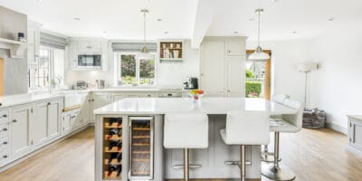 A white kitchen with stools and wine racks.