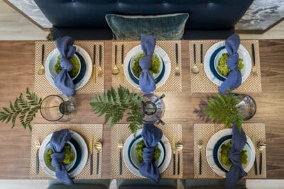 A dining table set with blue plates and ferns.