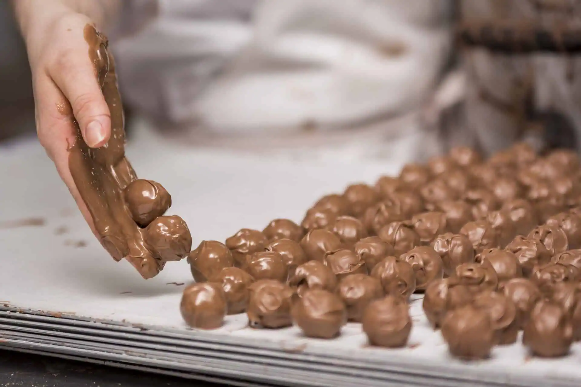 Hand dipping chocolate onto truffle chocolates in a confectionery production setting.